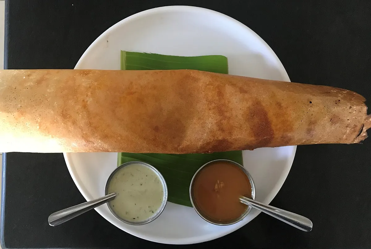 One rolled dosa on a plate with chutney and sambar